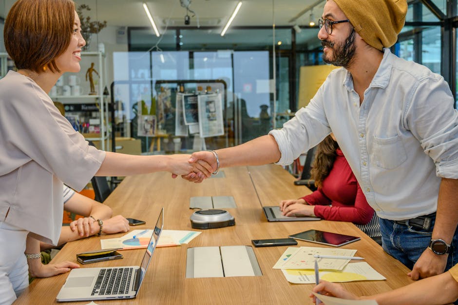 Diverse team in a modern office engaged in a collaborative meeting, sealing a partnership with a handshake.