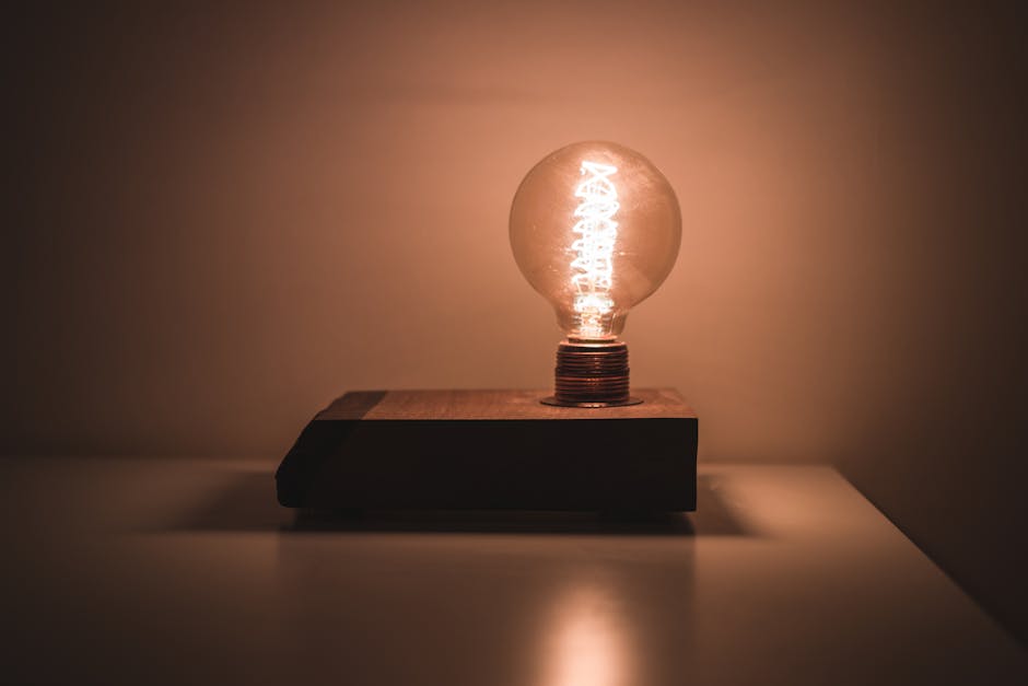 A glowing vintage-style lightbulb on a wooden base emits warm light in a dark room.