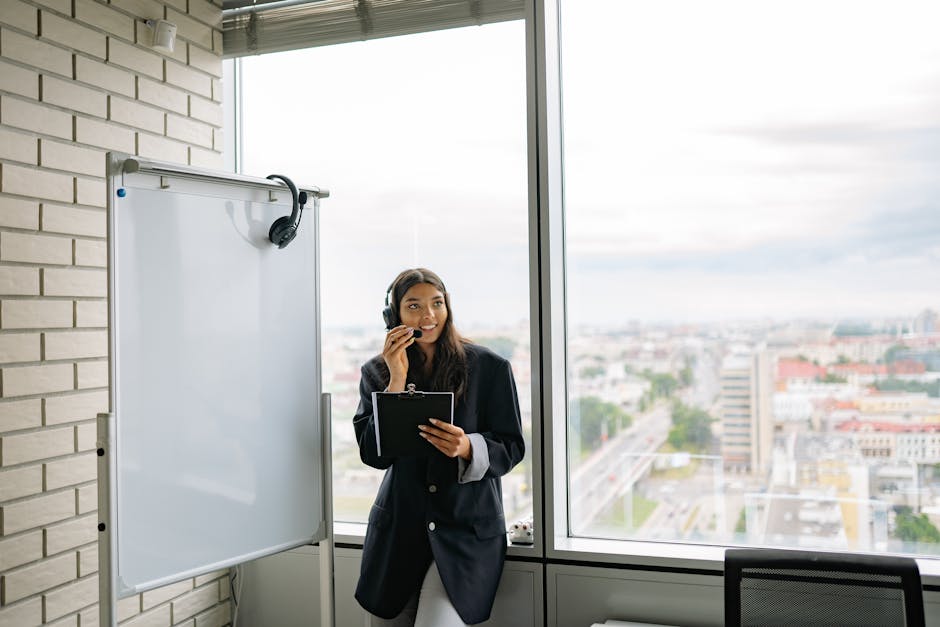Professional woman wearing headphones standing in a modern office with a city view. Ideal for business themes.